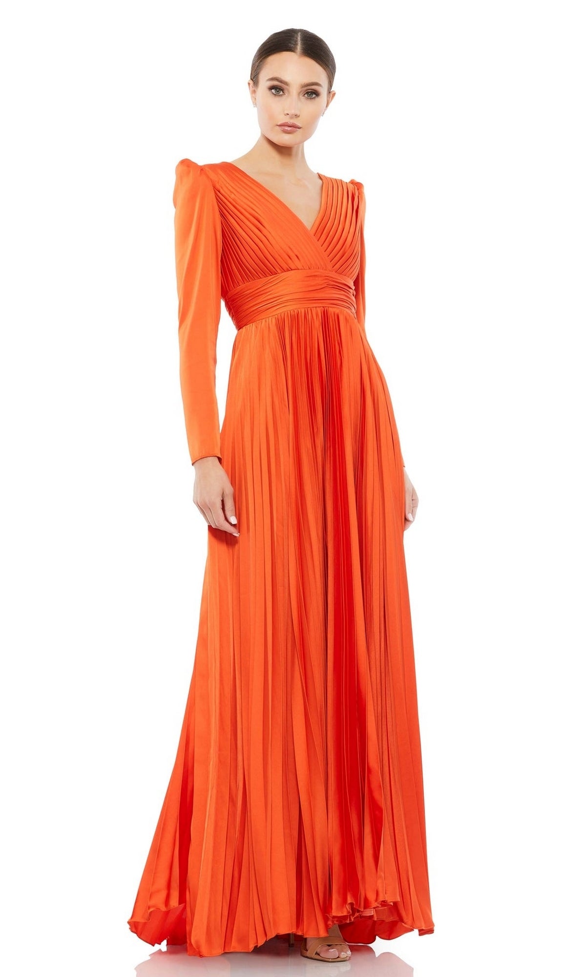 A woman poses elegantly against a white background in the Long Formal Dress 26542 by Mac Duggal—a floor-length, bright orange pleated gown with a V-neckline.